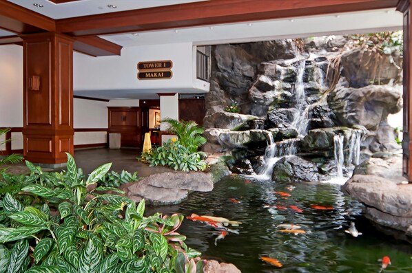 A hotel lobby with a koi pond, a waterfall, and a sign indicating 'Tower 1 Makai'.