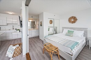 A modern bedroom with a large bed, a bedside table, a wicker chair, and a bathroom visible through an open door.