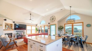 A spacious kitchen with a central island, a dining area with a large table, and a cozy seating area with a fireplace. - The Pup Deck - Duck, Carolina Dunes, 420 Yds to Beach, Pool, Hot Tub, Pets OK, Flex Stays (Duck)