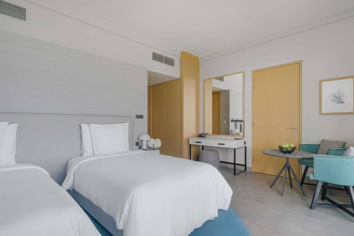 Ein Hotelzimmer mit zwei Betten, einem Schreibtisch, einem Stuhl und einem kleinen Tisch mit einer Obstschale.