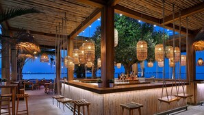 An outdoor bar area with wooden furniture and hanging wicker lamps. - Mövenpick Resort Al Marjan Island (Ras Al Khaimah)
