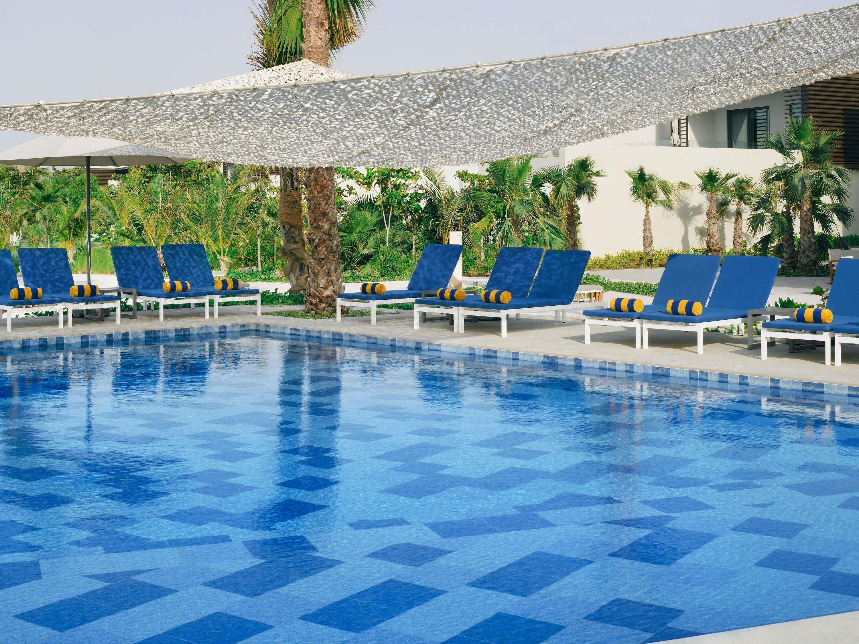 A swimming pool with blue tiles, surrounded by lounge chairs with yellow and black cushions.