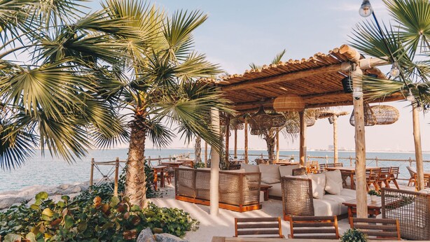 A beachside lounge with wicker furniture, a wooden deck, and a view of the sea. - M övenpick Resort Al Marjan Island (Ras Al Khaimah)