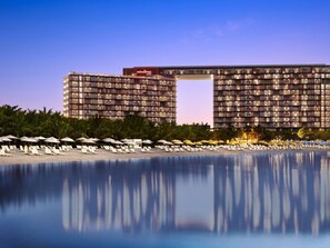Un hôtel à étages, doté d’une piscine et de chaises longues installées au bord de la plage.
