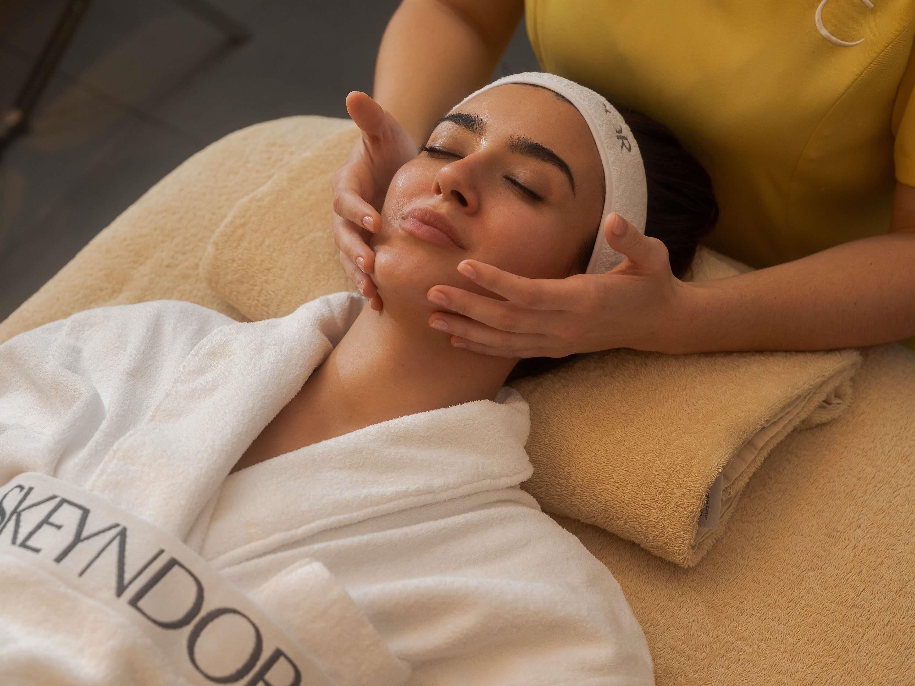 A person receiving a facial treatment in a room with a massage table and a towel.