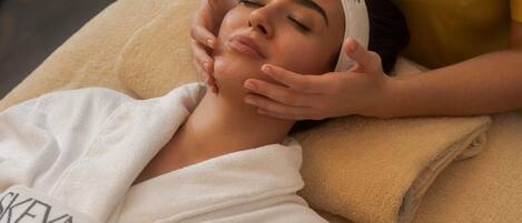 A person receiving a facial treatment in a room with a massage table and a towel.