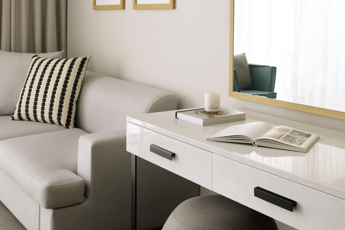 Une chambre d’hôtel moderne avec un canapé, une table de chevet sur laquelle se trouvent un livre et une bougie, et un miroir qui reflète la pièce.