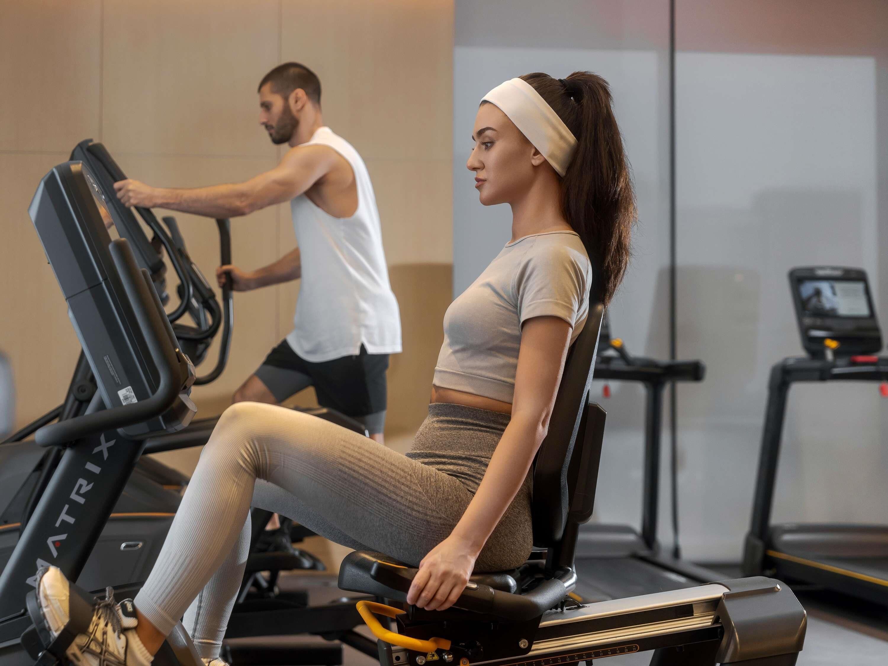 A gym with stationary bikes and treadmills, a man and a woman exercising.