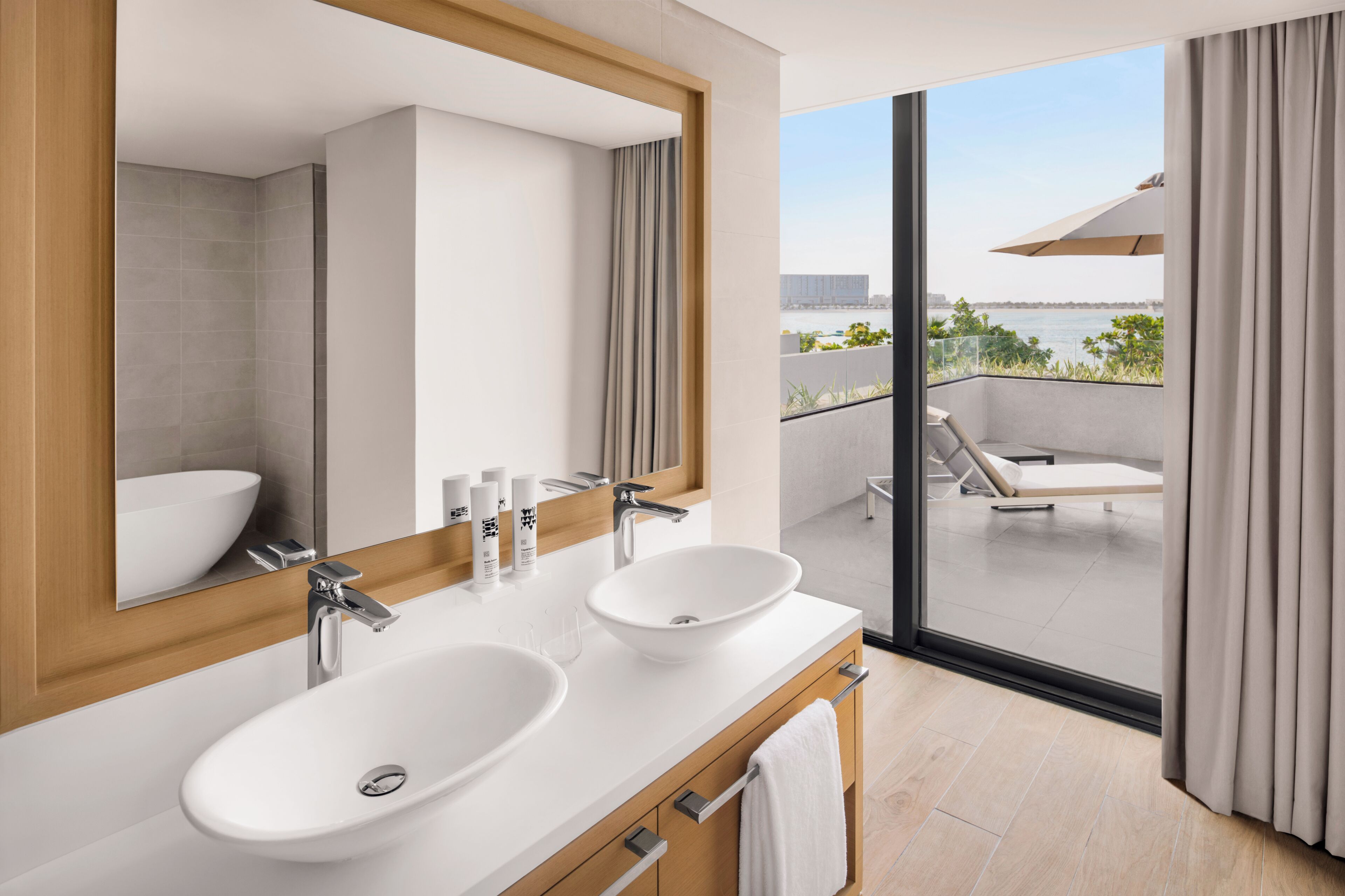 A modern bathroom with two sinks, a large mirror, and a view of a balcony with a pool.