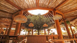 A circular wooden structure with a thatched roof, hanging woven light fixtures, and a central tree. - Mövenpick Resort Al Marjan Island (Ras Al Khaimah)