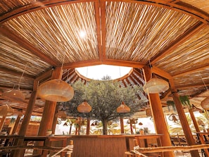 A circular wooden structure with a thatched roof, hanging woven light fixtures, and a central tree. - Mövenpick Resort Al Marjan Island (Ras Al Khaimah)