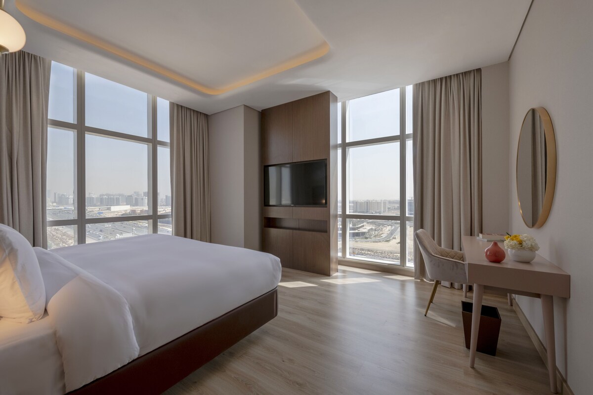 Une chambre d’hôtel moderne, dotée d’un grand lit, d’un bureau, d’une télévision et offrant une vue sur la ville.