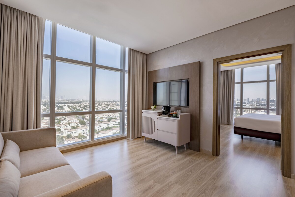 Une chambre d’hôtel moderne dotée d’une grande fenêtre, d’un téléviseur à écran plat, d’un lit, d’un canapé et d’un petit bureau.