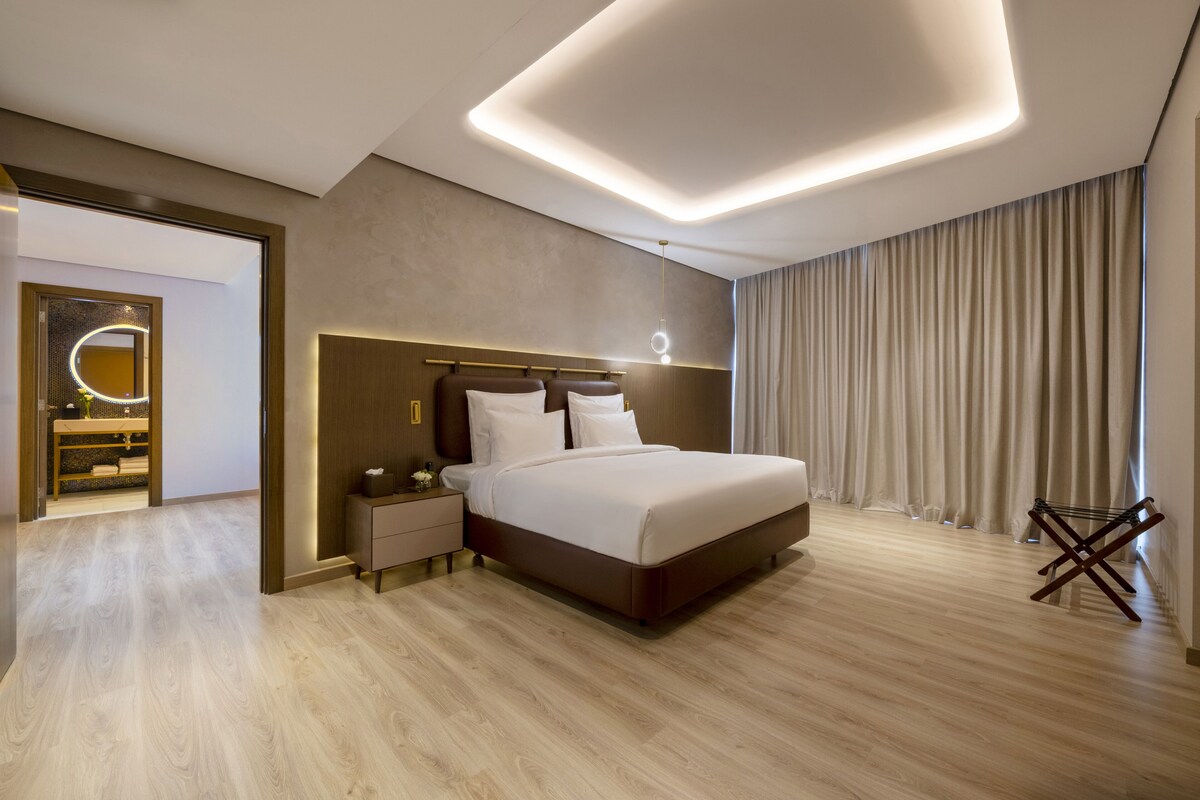 Une chambre à coucher moderne avec un grand lit, des tables de chevet, un miroir et une vue sur l’extérieur.