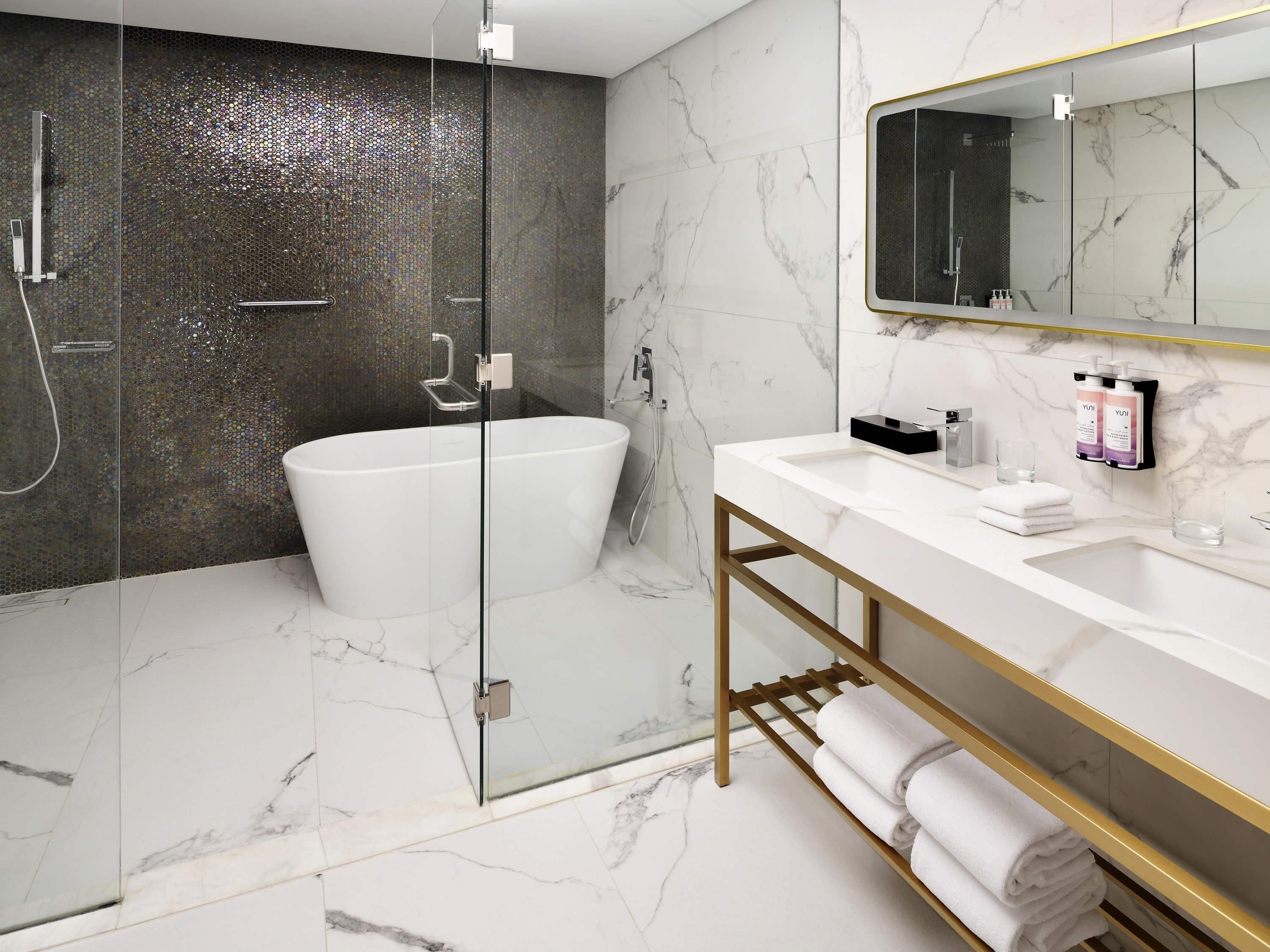 Une salle de bain moderne dotée d’une douche à parois de verre, d’une baignoire sur pieds et d’un meuble-lavabo avec un cadre doré.