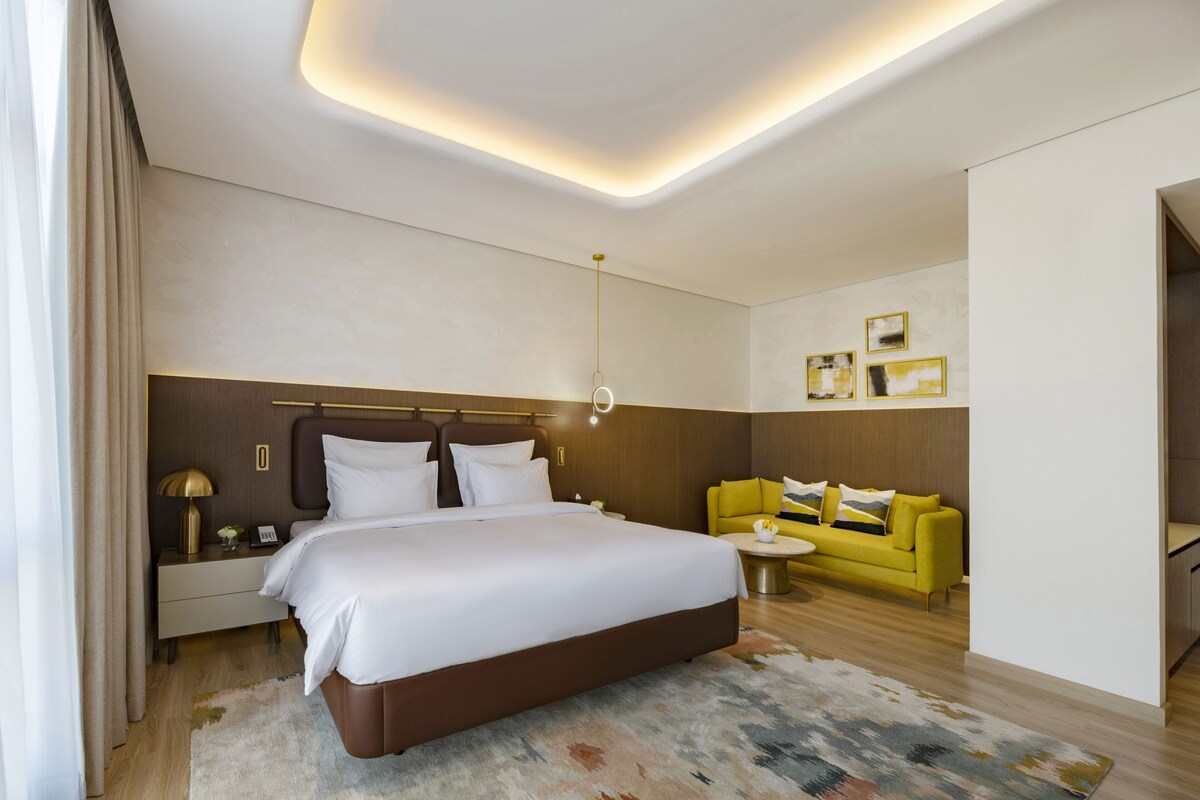 Une chambre d’hôtel moderne avec un grand lit, un canapé jaune et une petite table ronde.