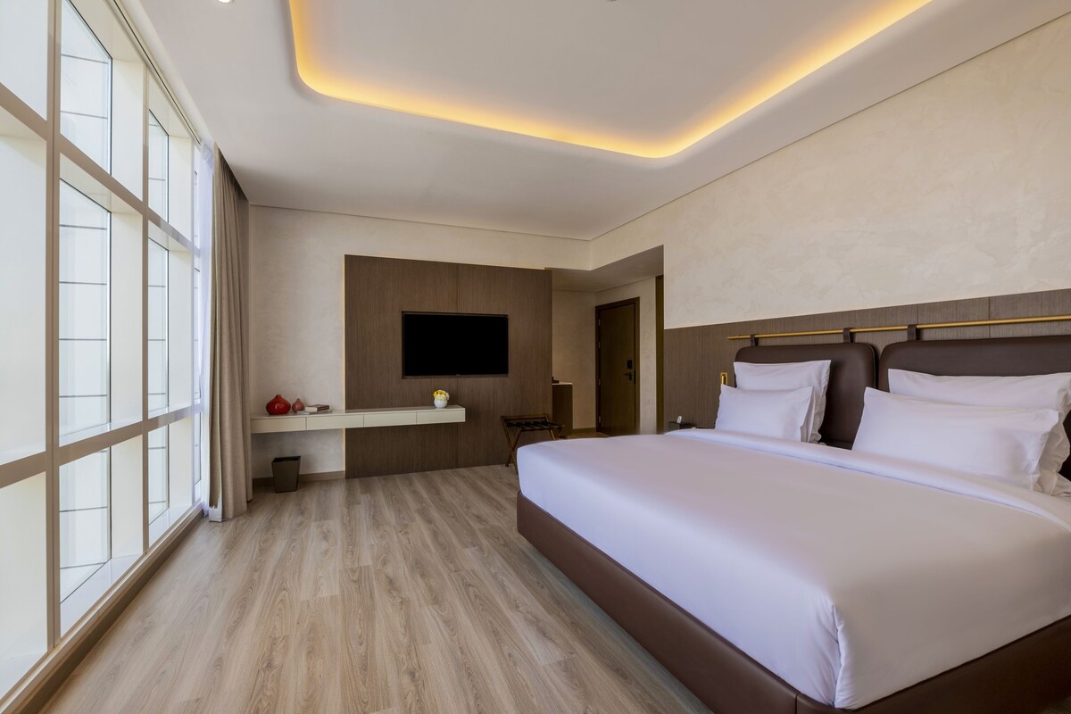 Une chambre d’hôtel moderne dotée d’un grand lit, d’un téléviseur à écran plat fixé au mur et d’un plancher en bois.