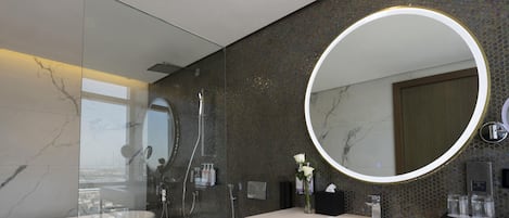A modern bathroom with a glass-enclosed shower, a large round mirror, and a marble-tiled vanity.