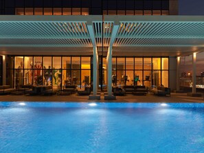 Een modern hotel met een zwembadgedeelte, buitenzitplaatsen en zichtbare fitnessapparatuur door grote ramen.
