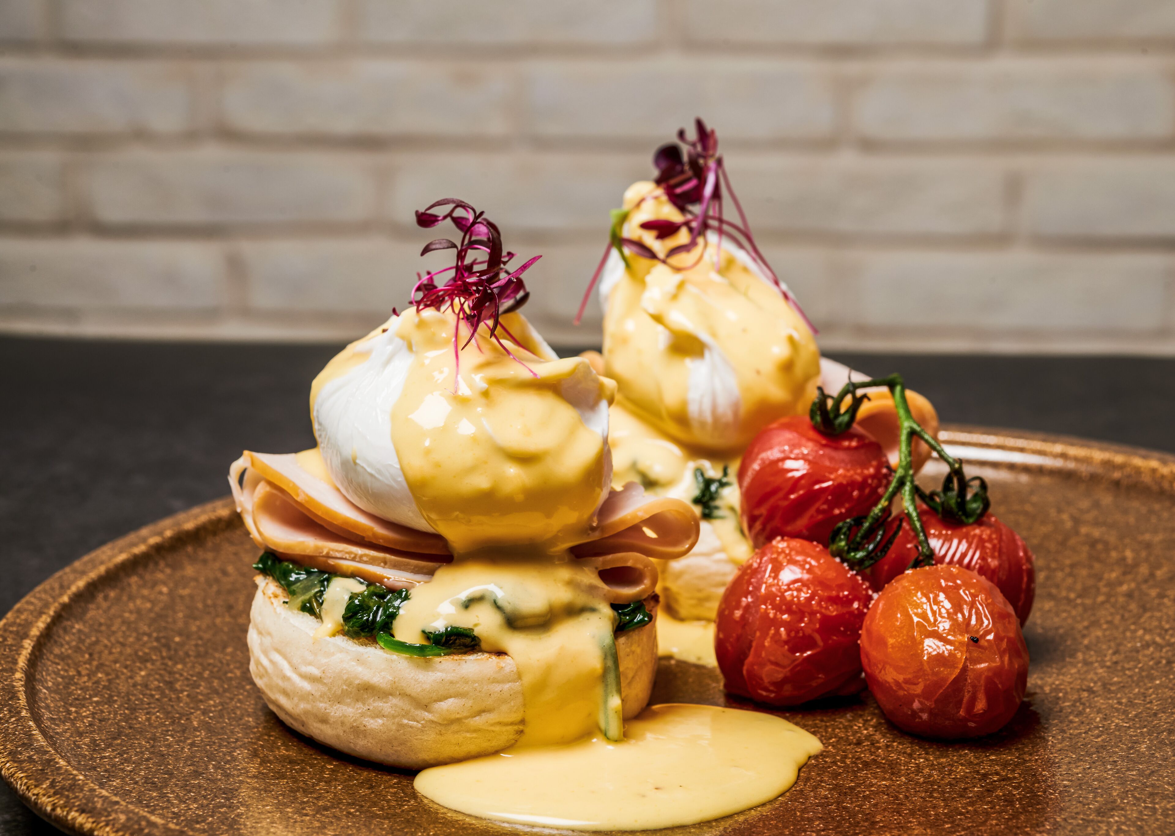 Un plato de comida con huevos benedictinos, jamón, espinacas y tomates cherry.