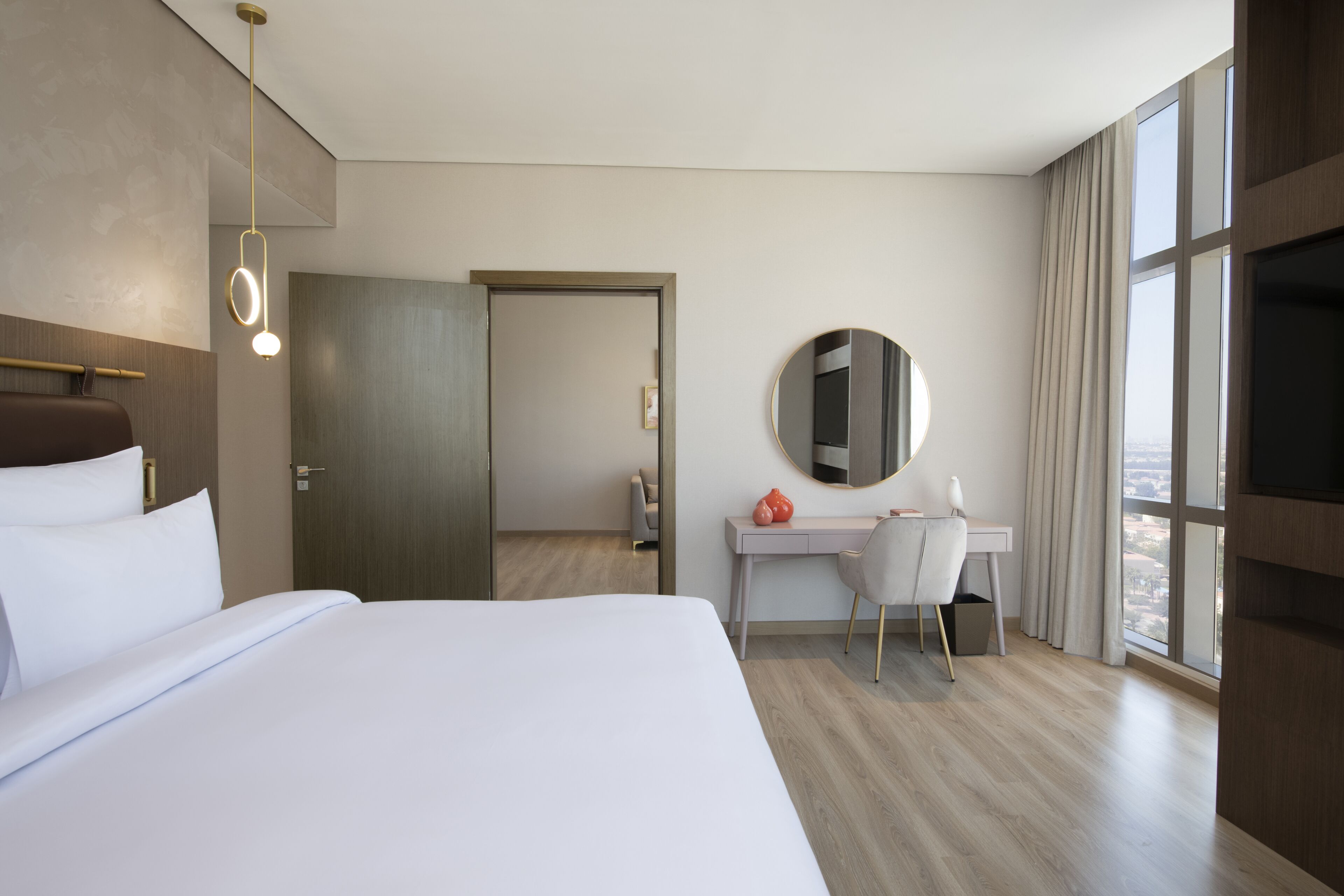 A hotel room with a large bed, a desk with a chair, a round mirror, and a TV.