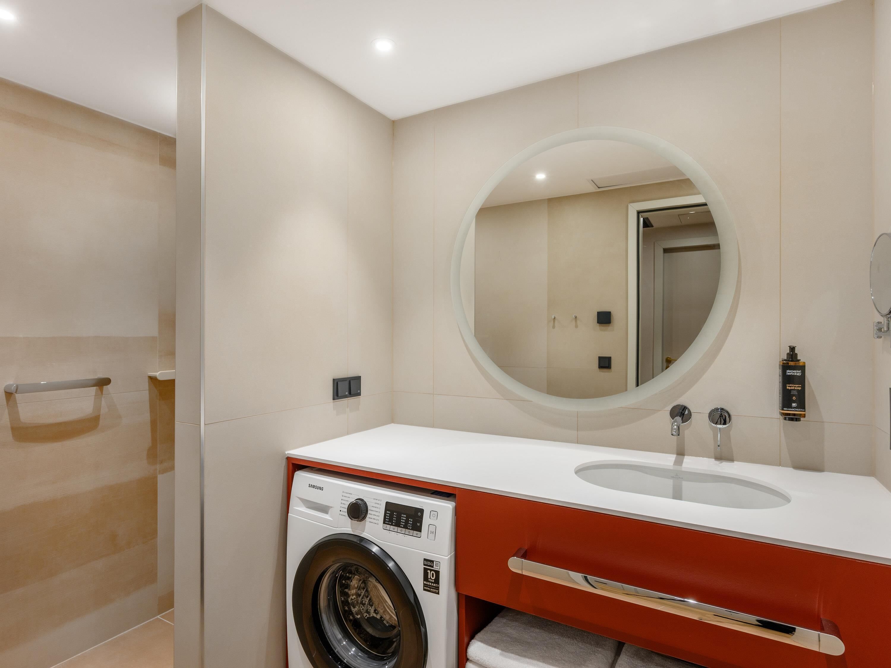 A modern bathroom with a washing machine, a sink, and a mirror.