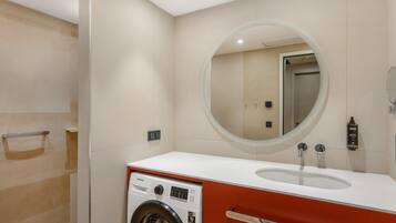 A modern bathroom with a washing machine, a sink, and a mirror.