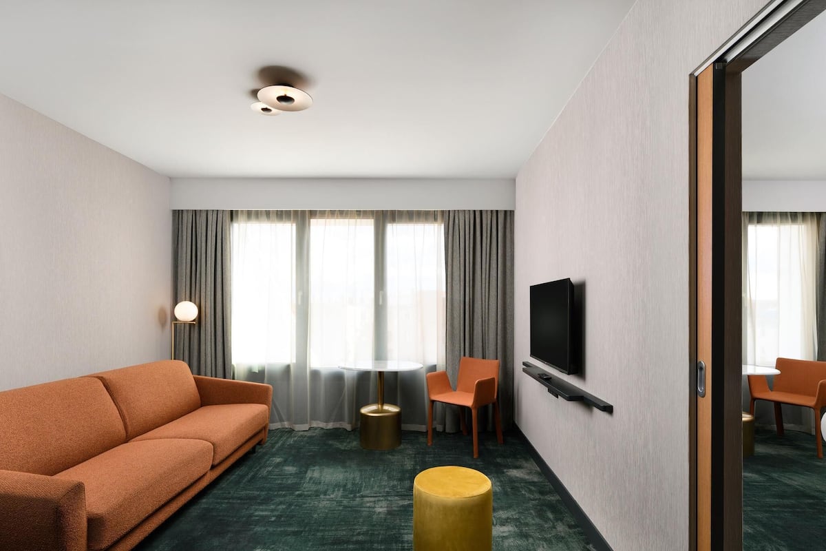 A hotel room with a sofa, chairs, a TV, a small table, and a round stool.