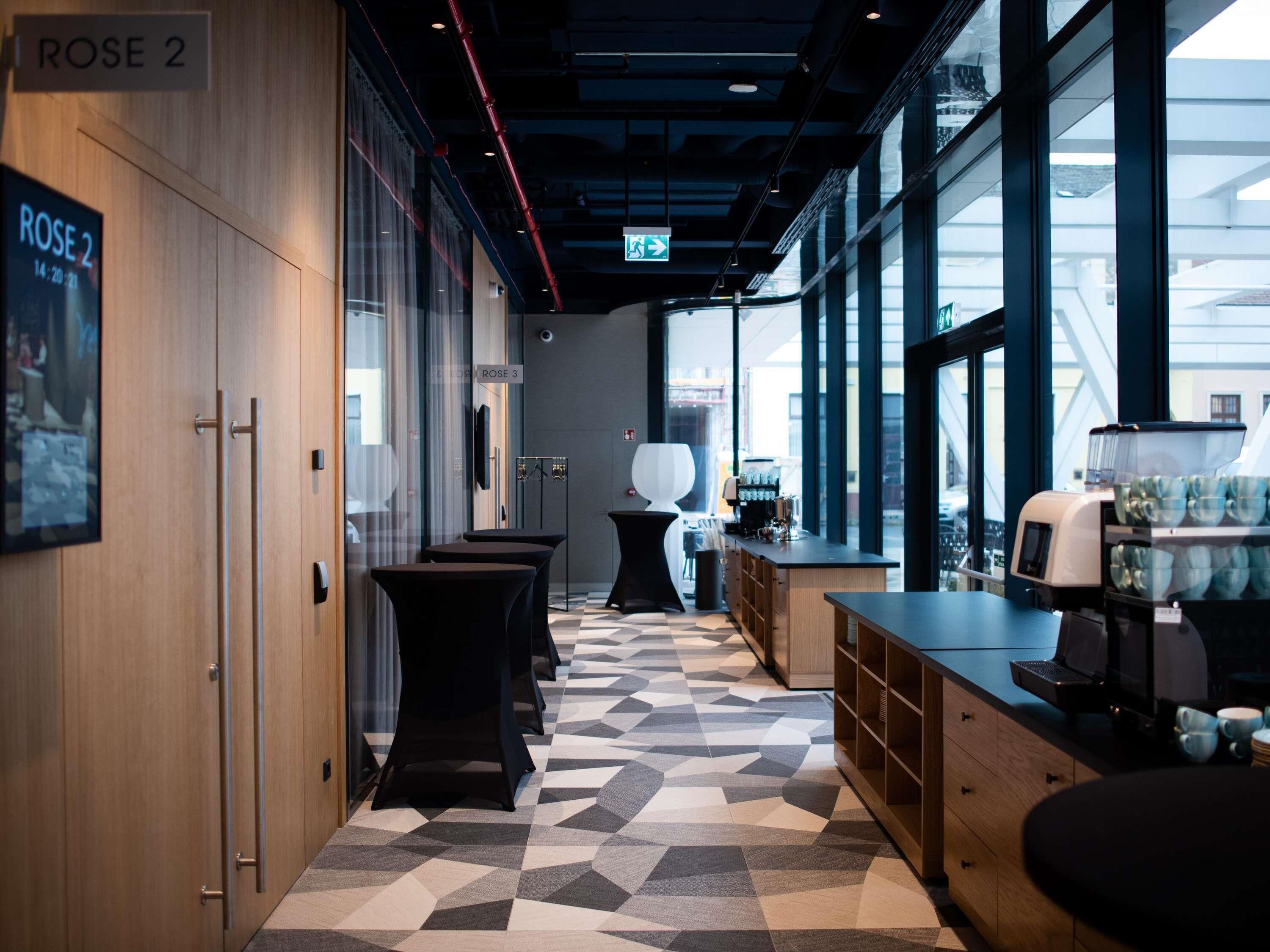 A modern interior with a geometric patterned floor, a coffee station, and large windows.