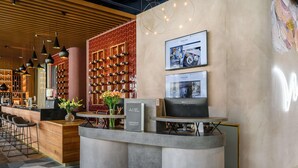 A modern hotel lobby with a reception desk, bar area, wine rack, and a large screen displaying content.