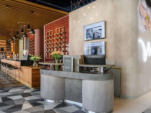 A modern hotel lobby with a reception desk, bar area, wine rack, and a large screen displaying content. - Mercure Debrecen (Debrecen)