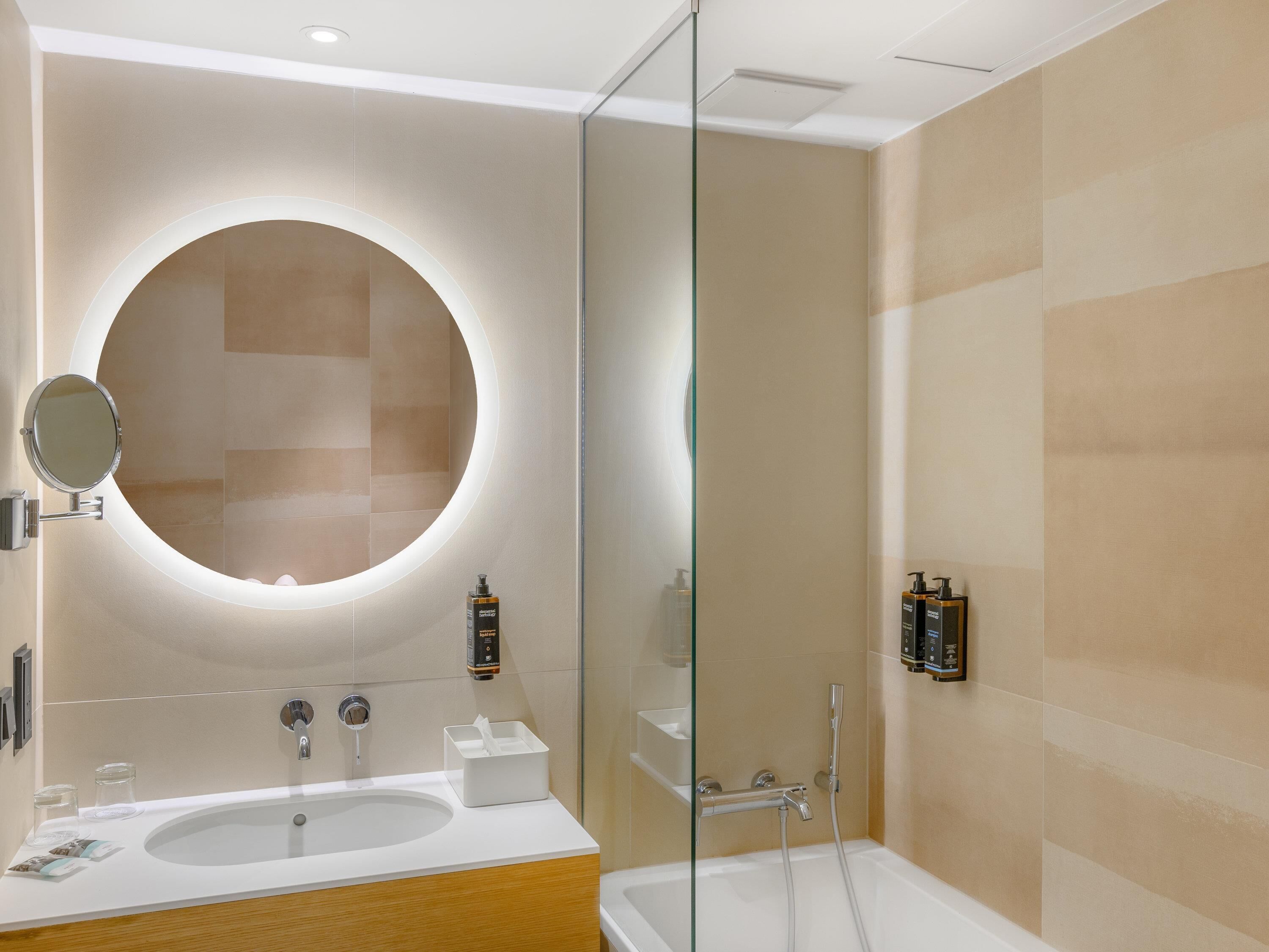 A modern bathroom with a round mirror, a bathtub, and a glass-enclosed shower.