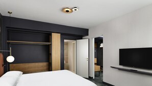 A modern hotel room with a bed, a TV mounted on the wall, a wardrobe, and a door leading to a bathroom.