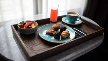 Uma bandeja com itens de café da manhã, incluindo croissants, muffins e uma tigela de frutas, além de uma xícara de café e um copo de suco.