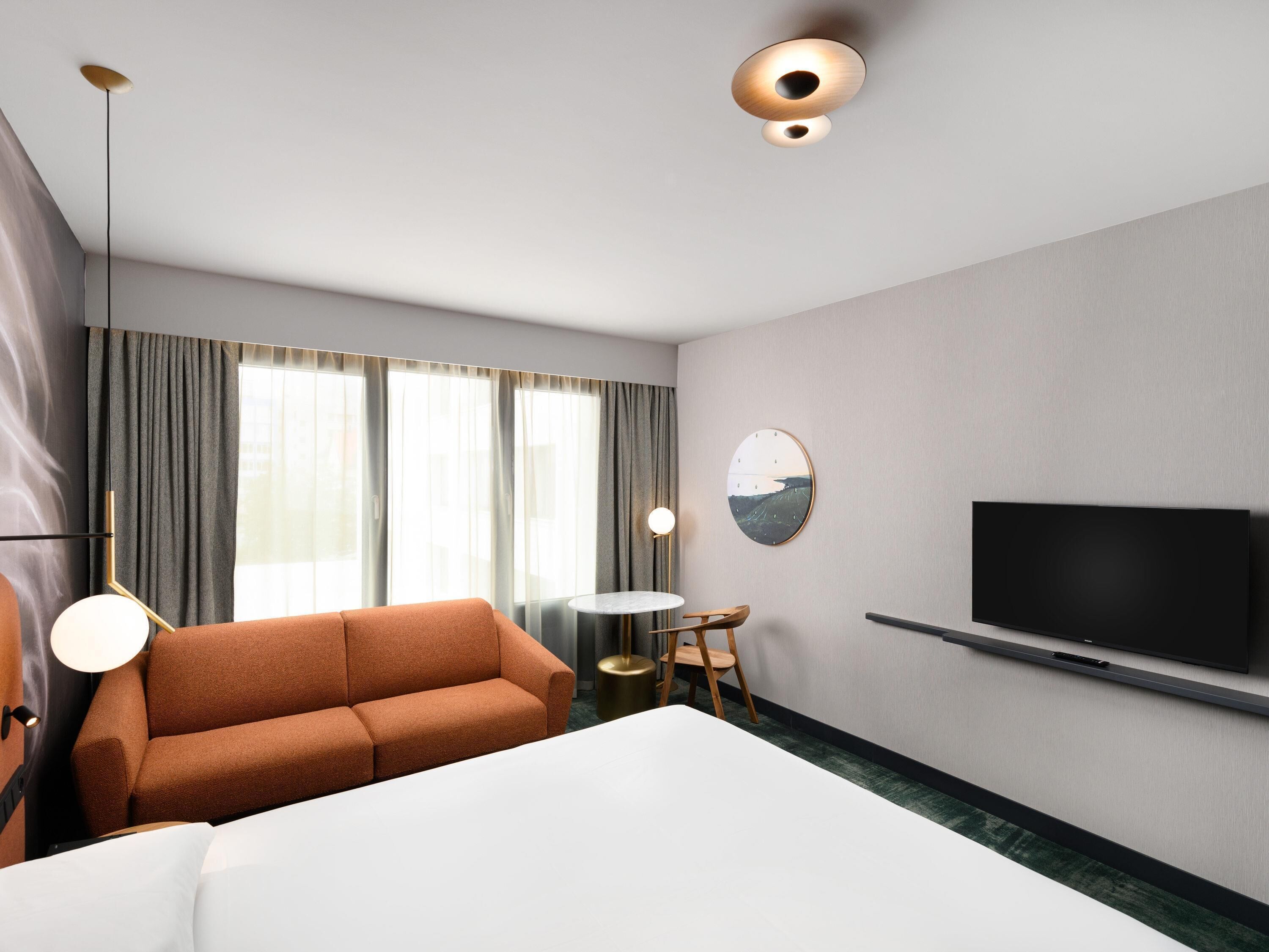 Una habitación de hotel con una cama grande, un sofá, un televisor y una mesa de comedor.