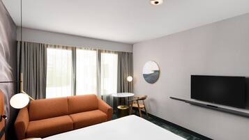 Una habitación de hotel con una cama grande, un sofá, un televisor y una mesa de comedor.