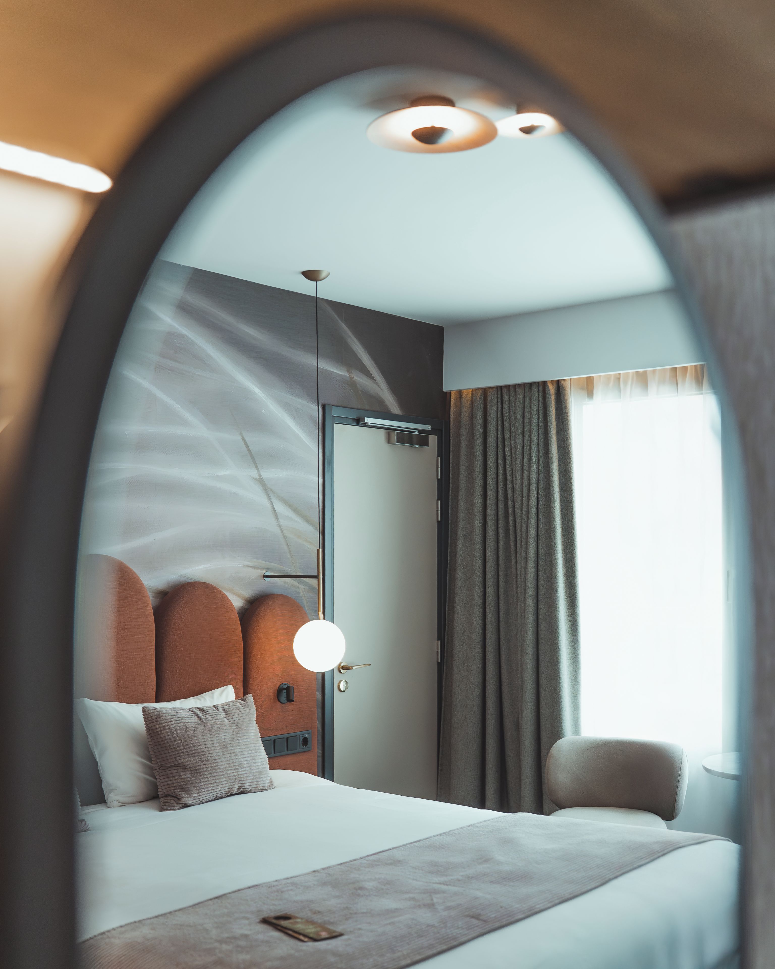 A modern hotel room with a bed, a bedside table, a chair, and a large window.
