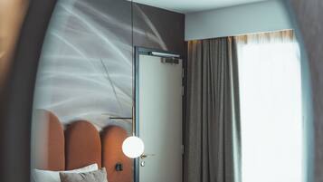 A modern hotel room with a bed, a bedside table, a chair, and a large window.