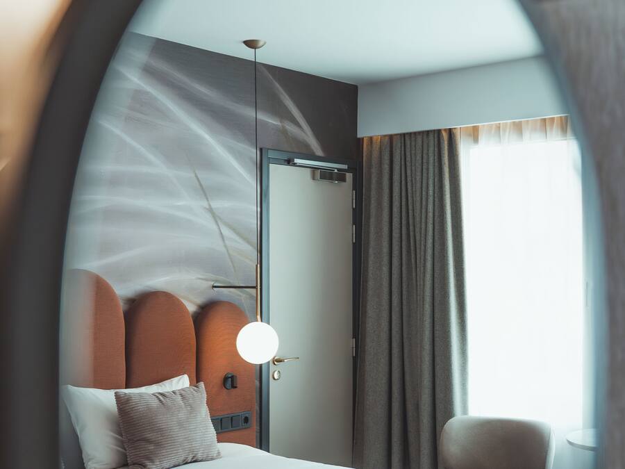 A modern hotel room with a bed, a bedside table, a chair, and a large window.