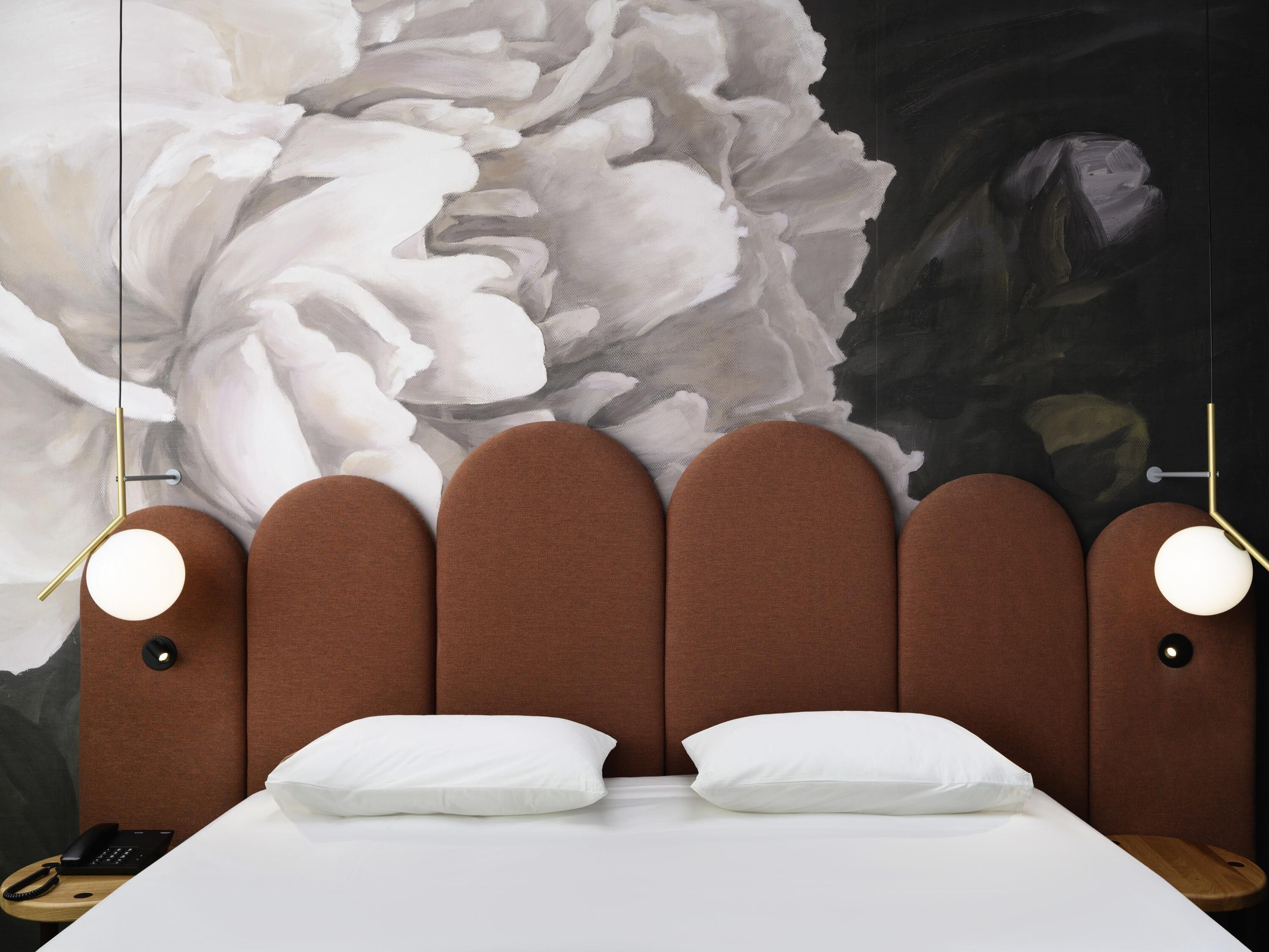 Una cama con cabecera tapizada en tono marrón, almohadas blancas y lámparas de noche.