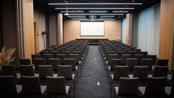 Un salón de conferencias con filas de sillas, una pantalla de proyector y suelo alfombrado.