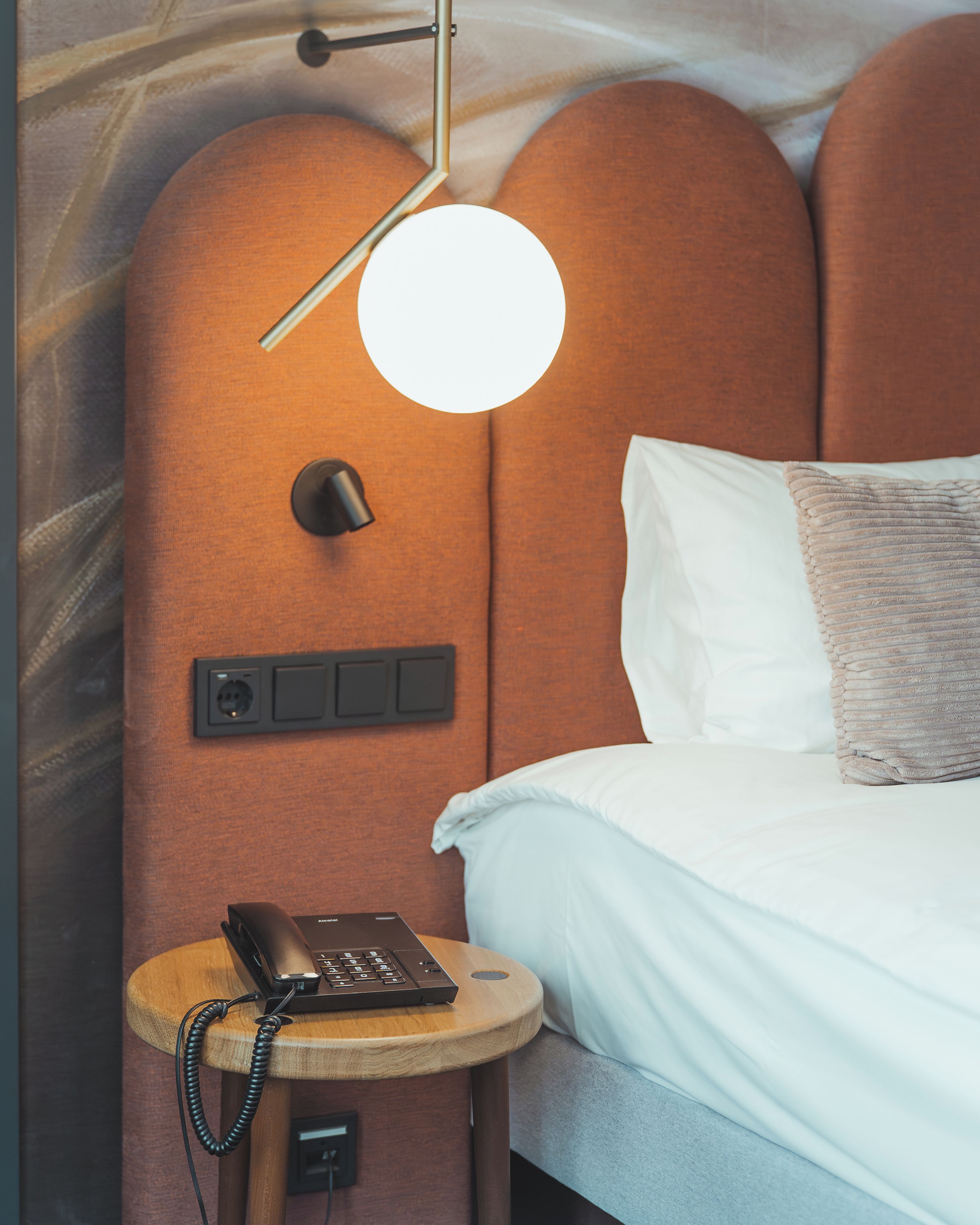 Una camera d'albergo con un letto, un comodino con il telefono, una presa elettrica e un quadro elettrico.