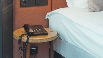 Una camera d'albergo con un letto, un comodino con il telefono, una presa elettrica e un quadro elettrico.