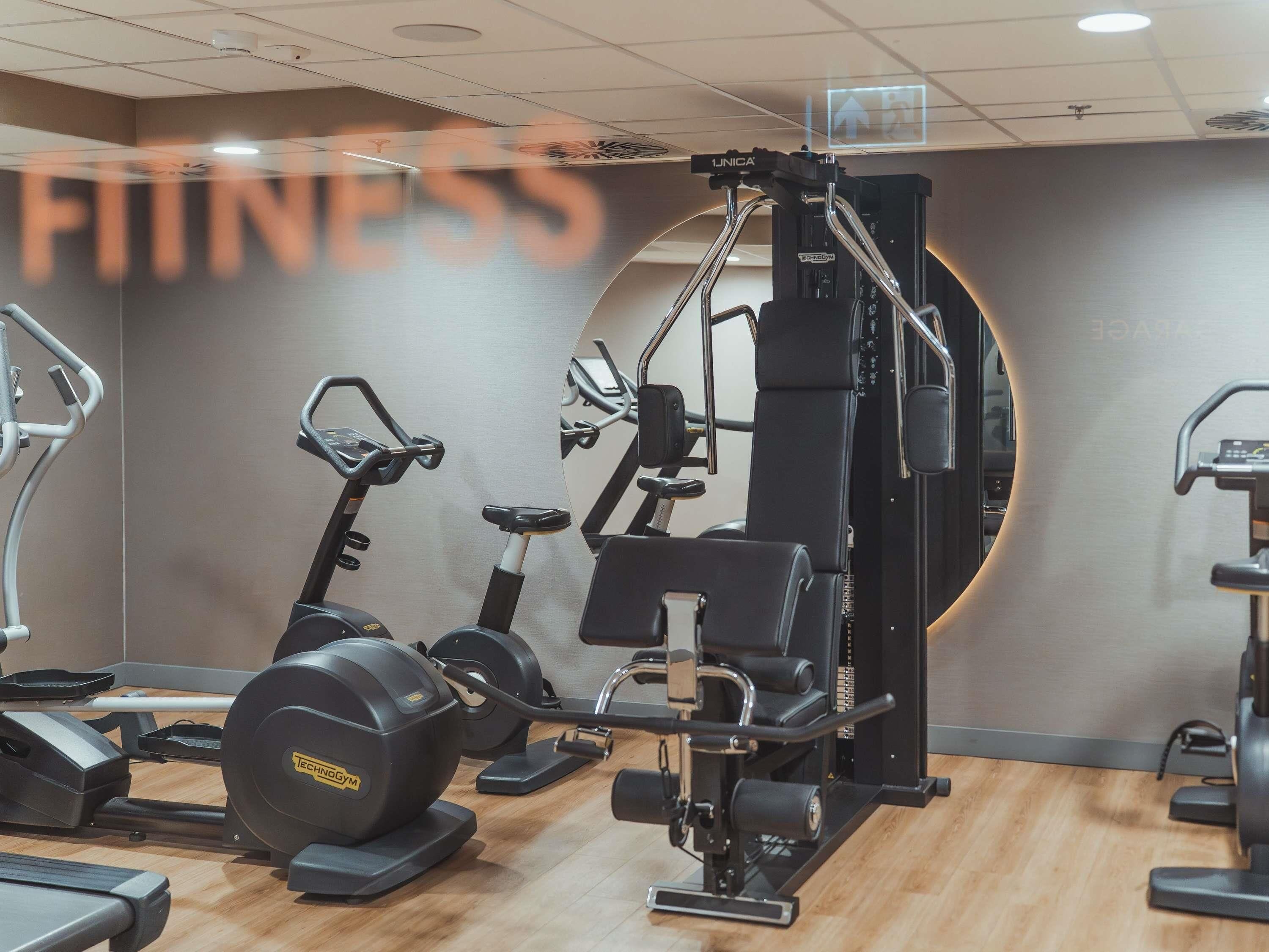 Una palestra con macchinari cardio, attrezzature per sollevamento pesi e uno specchio a parete.