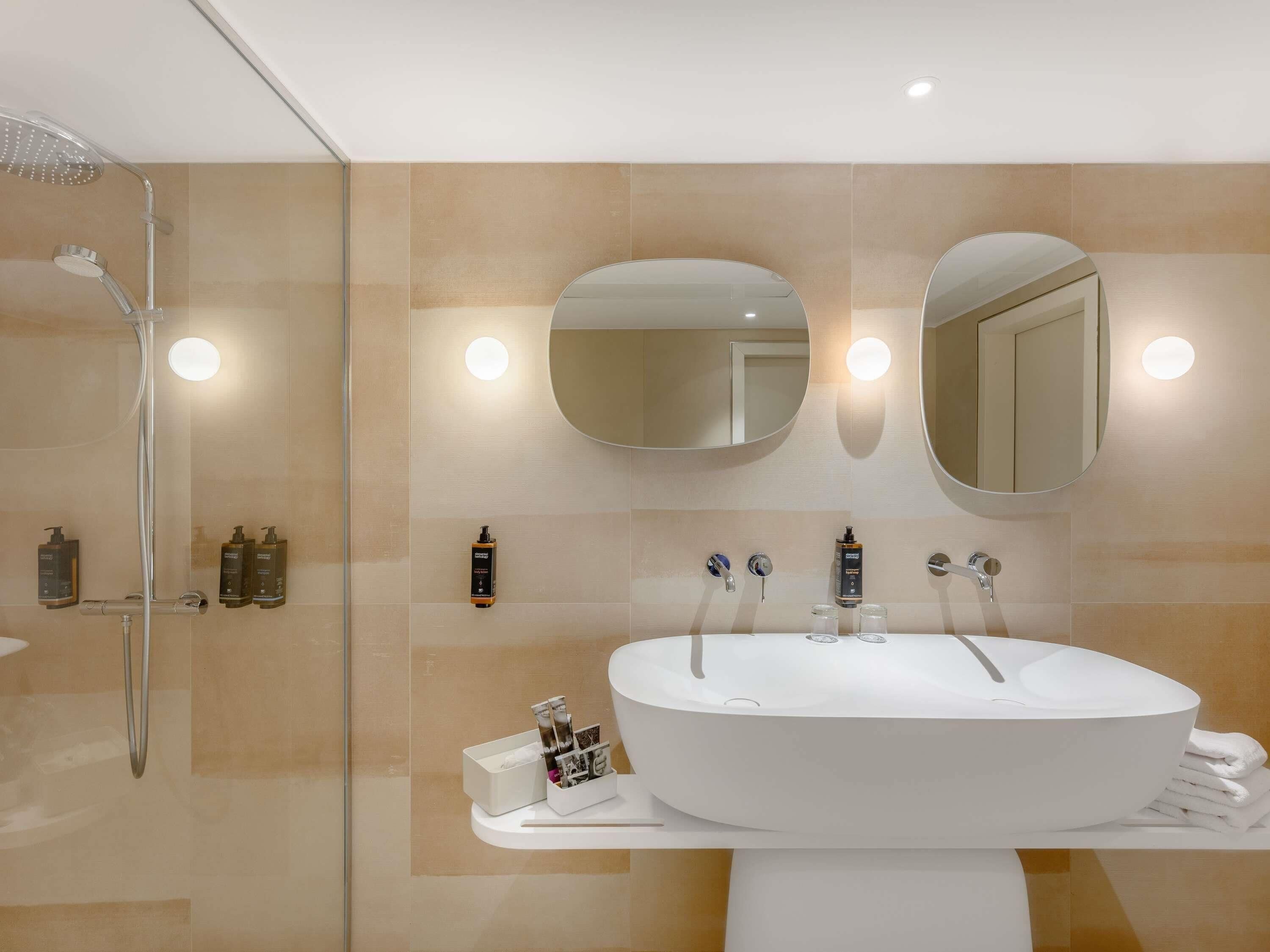 A modern bathroom with a freestanding bathtub, two wall-mounted mirrors, and a glass shower enclosure.