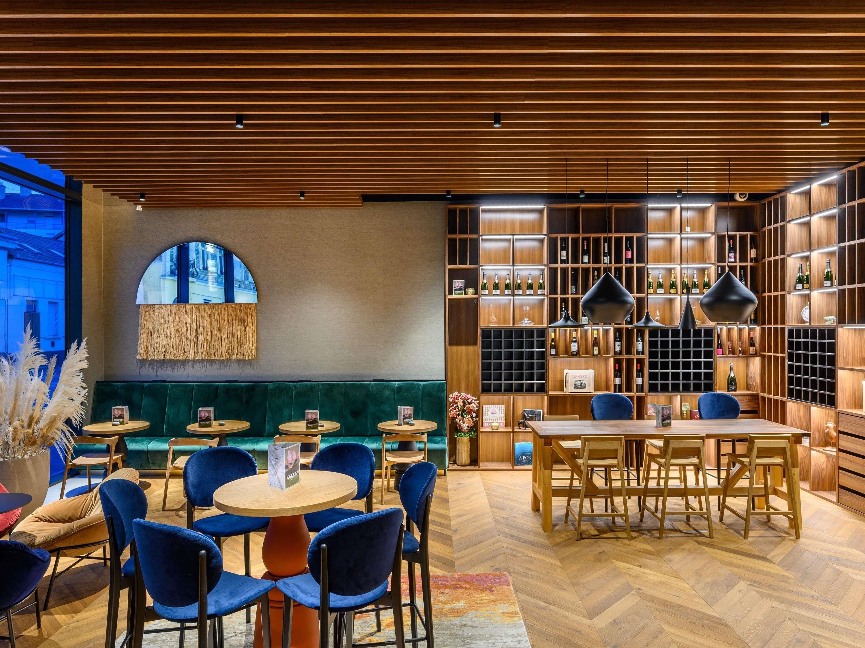 A restaurant with wooden ceiling, green seating, and wine racks.