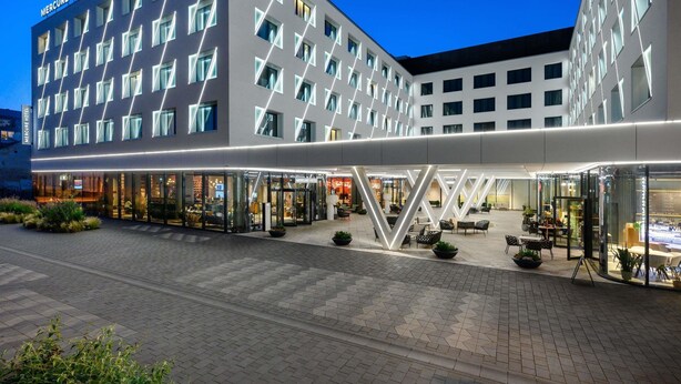 A modern hotel with a geometric facade, multiple balconies, and outdoor seating areas.
