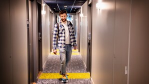 A man skateboarding down a hallway with patterned carpet and doors on either side. - Ibis Budget Reims Parc Des Expositions (Reims)