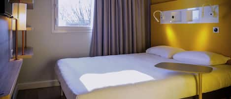 Habitación de hotel con cama, mesita de noche, lámpara, ventana con cortinas y aplique de pared.