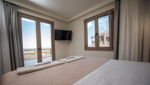 Ein Hotelzimmer mit einem großen Bett, einem flachbildfernseher an der Wand und einem Balkon mit Meerblick.